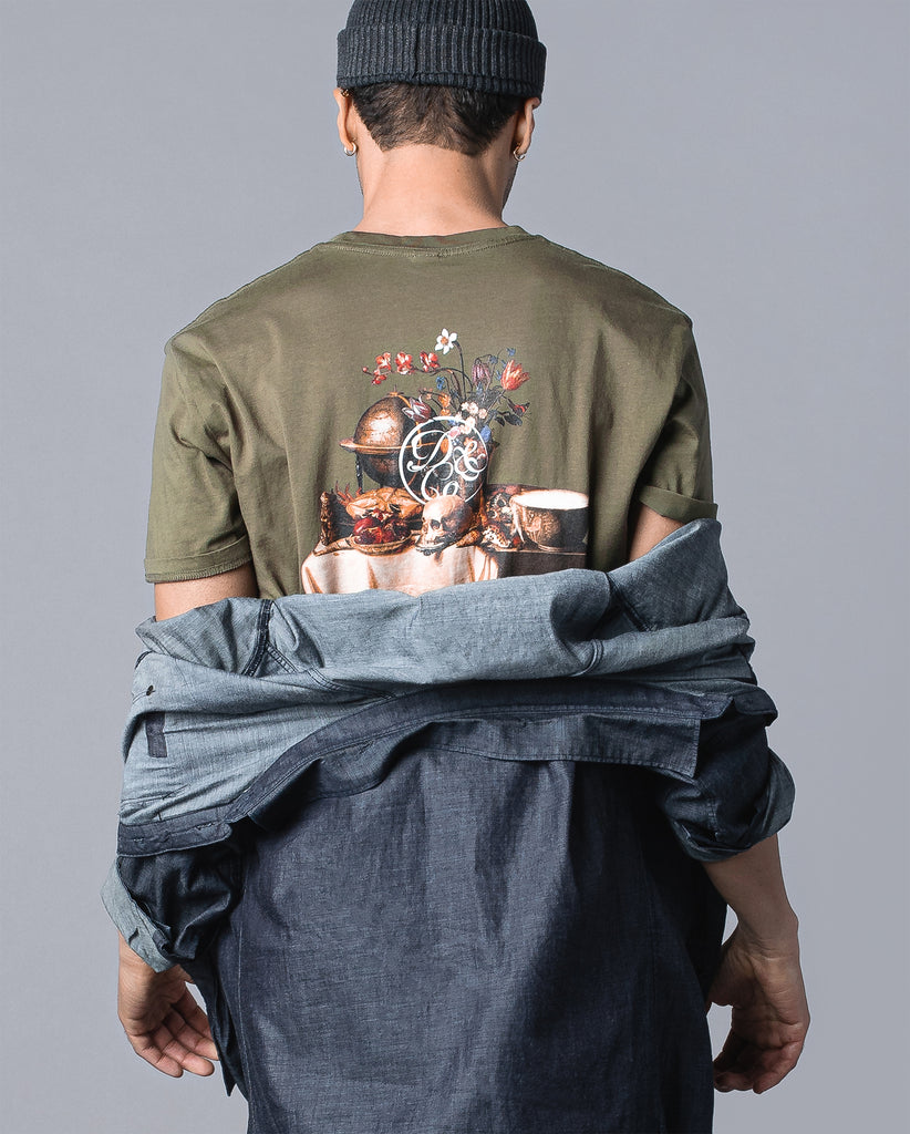 back of man wearing olive tee with table of food and drinks graphic and death & co. logo
