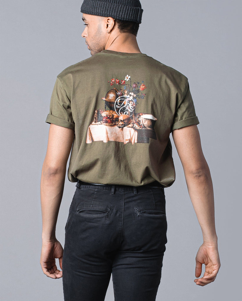 back of man wearing olive tee with table of food and drinks graphic and death & co. logo