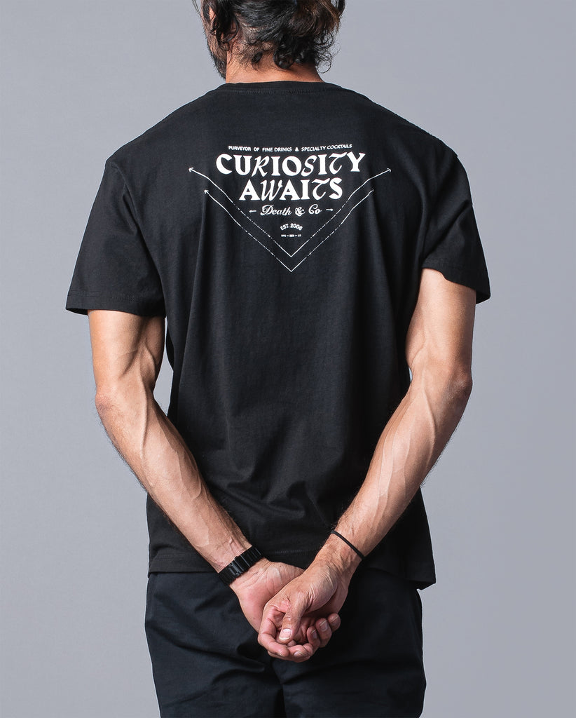 back of man wearing black t-shirt with "curiosity awaits" 