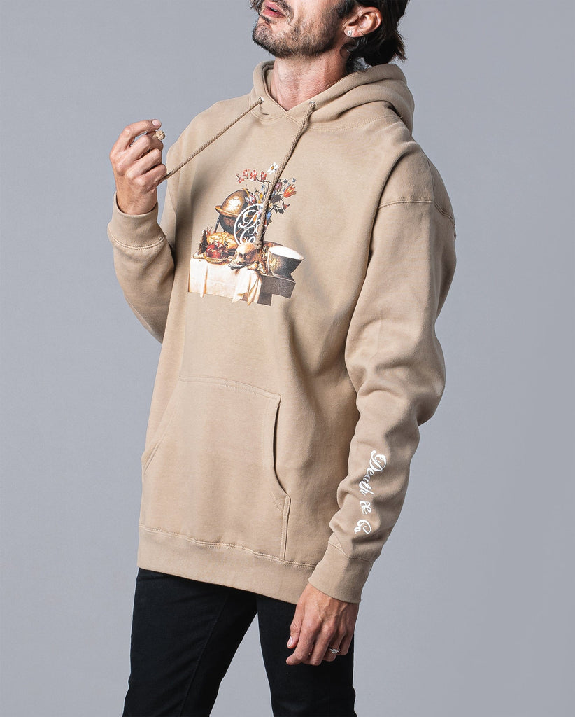 man wearing tan hoodie with table of food and drinks graphic and death & co. logo