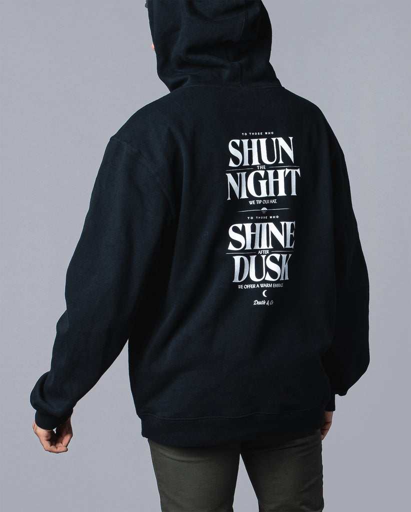 back of man wearing black hoodie with "to those who shun the night we tip our hat. To those who shine after dusk we offer a warm embrace"