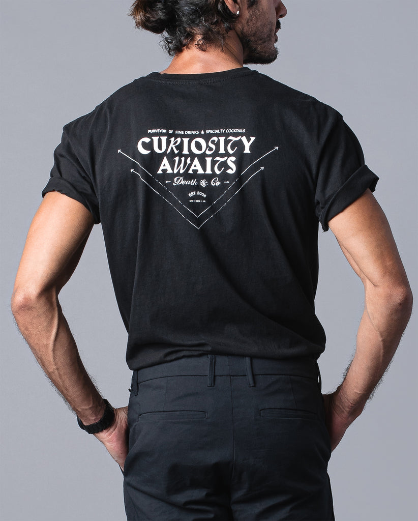 back of man wearing black t-shirt with "curiosity awaits" 